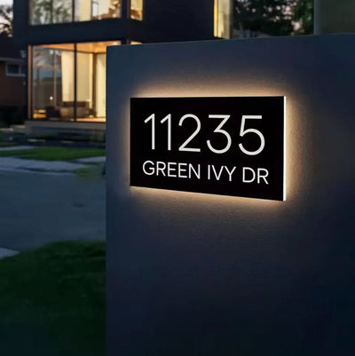 Modern house number sign with illuminated text on a wall outside a building.